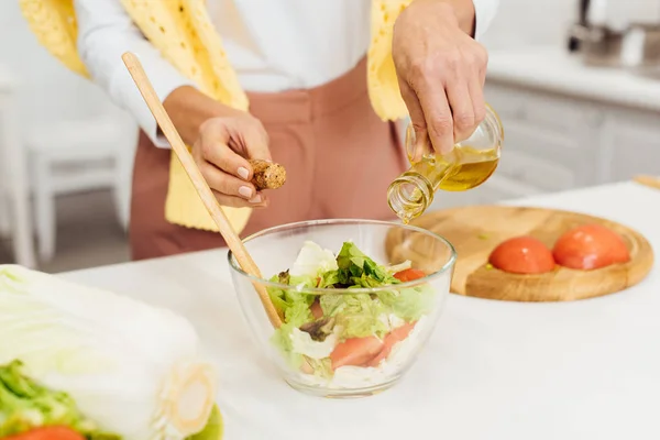 Gros plan des mains féminines verser de l'huile dans la salade sur la table — Photo de stock