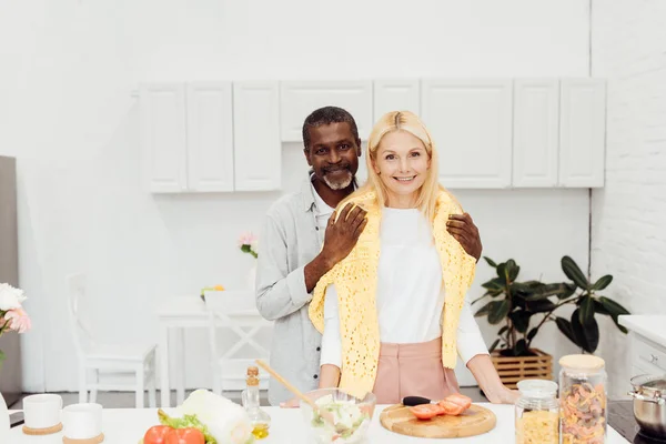 Casal sorrindo cozinhar jantar e abraçar na cozinha — Fotografia de Stock