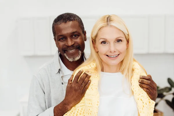 Feliz africano americano hombre abrazando sonriente rubia mujer - foto de stock