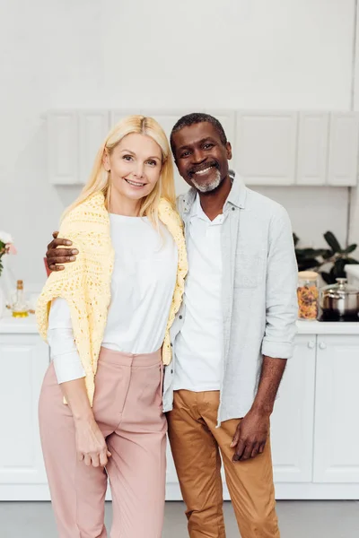 African american man embracing blonde mature woman at kitchen — Stock Photo