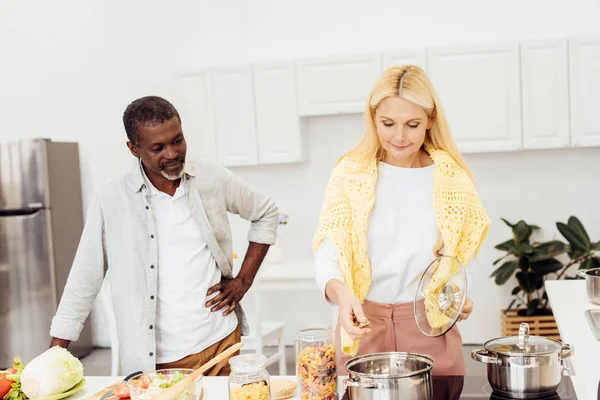 African american man watching blonde woman cooking dinner — Stock Photo
