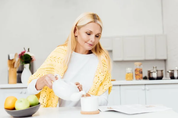 Donna sorridente seduta in cucina e bere tè al mattino — Foto stock