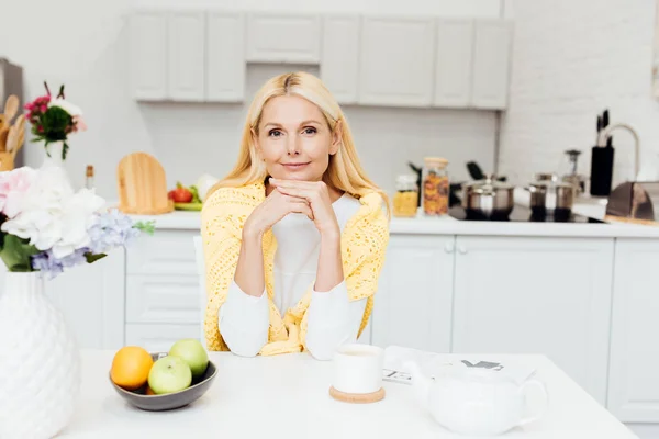 Donna sorridente seduta in cucina e bere tè al mattino — Foto stock