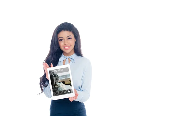 Красива афроамериканська дівчина тримає цифровий планшет з додатком квитків і посміхається на камеру ізольовано на білому — стокове фото