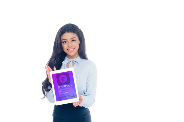 Hermosa chica afroamericana sosteniendo tableta digital con aplicación de compras y sonriendo a la cámara aislada en blanco - foto de stock