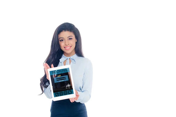 Hermosa chica afroamericana sosteniendo tableta digital con aplicación de reserva y sonriendo a la cámara aislada en blanco - foto de stock