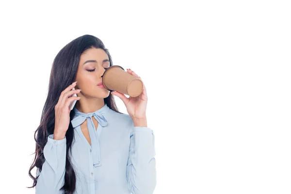 Joven mujer de negocios afroamericana bebiendo café de la taza de papel y hablando por teléfono inteligente aislado en blanco - foto de stock