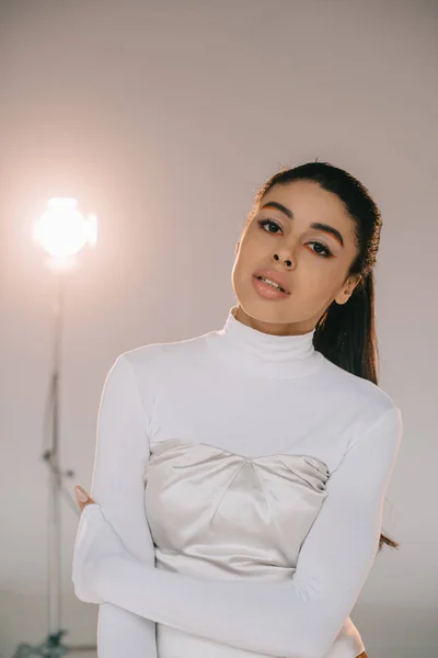 Pretty african american girl in white turtle neck looking at camera in studio with spotlight — Stock Photo