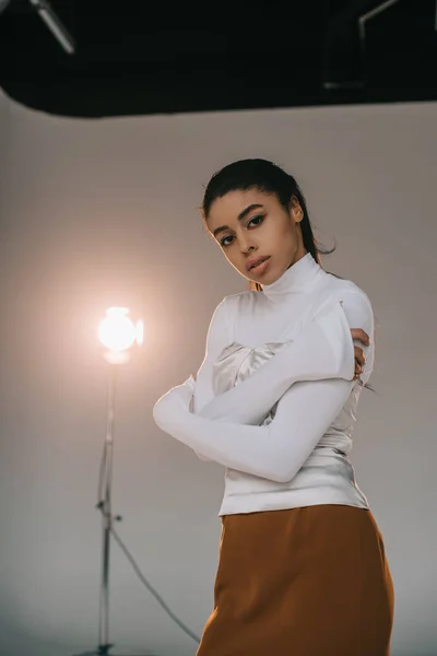 Modelo femenino afroamericano con estilo en cuello de tortuga blanca mirando a la cámara en el estudio con foco - foto de stock