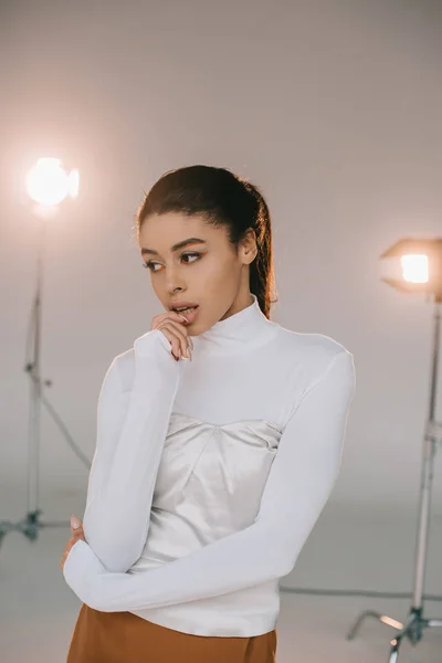 Attractive african american girl in white turtle neck looking away in studio with spotlights — Stock Photo