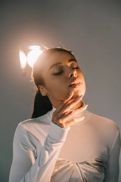 Молода афроамериканська жіноча модель в білій черепасі позує із закритими очима в студії з прожектором — стокове фото