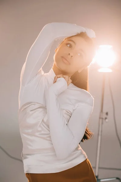 Selective focus of african american girl in white turtle neck posing in studio with spotlight — Stock Photo