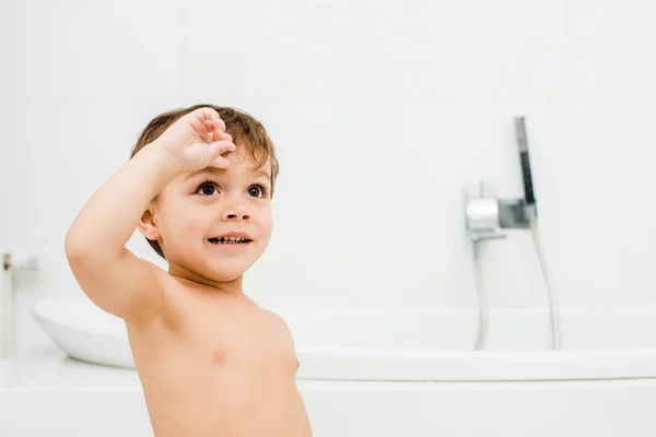 Tout-petit garçon regardant surpris et souriant dans la salle de bain blanche — Photo de stock