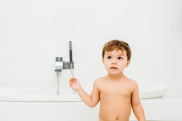 Маленький мальчик окрашивается и смотрит на что-то в белой ванной комнате — стоковое фото