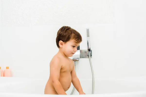 Tout-petit garçon debout et regardant vers le bas dans la salle de bain blanche — Photo de stock