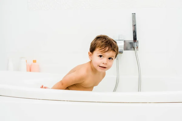 Lindo chico jugando y inclinándose en el baño blanco - foto de stock
