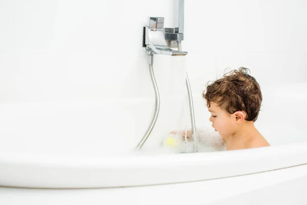 Menino criança sentado no banheiro branco e brincando com brinquedos de banho — Fotografia de Stock