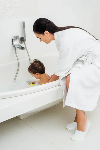 Mère en peignoir lavage fils dans la salle de bain — Photo de stock