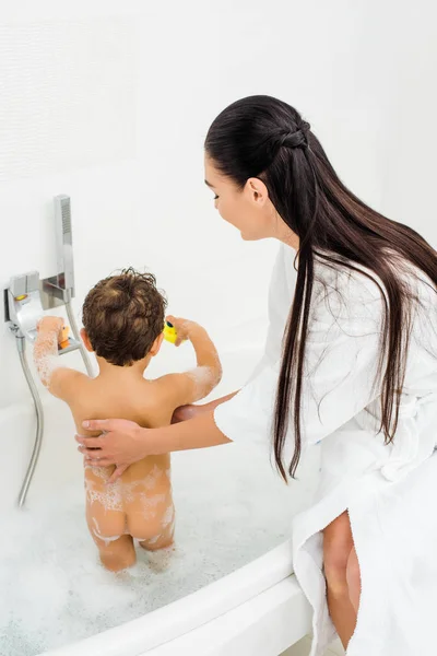 Мать с длинными волосами стиральный сын в белой ванной комнате — стоковое фото