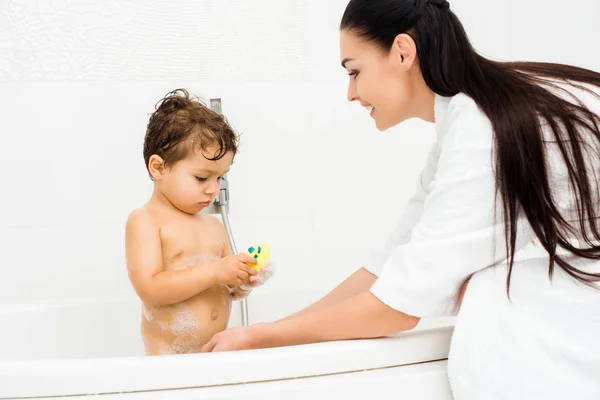 Madre lavaggio figlio con giocattolo bagno giallo — Foto stock