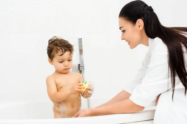 Mother washing son with yellow toy in white bathroom — Stock Photo