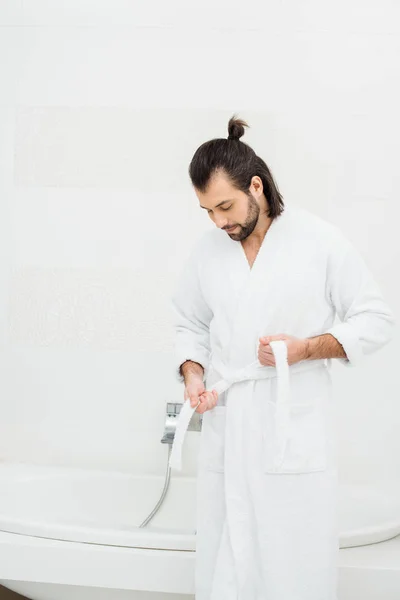 Hombre guapo desatando albornoz en baño blanco - foto de stock