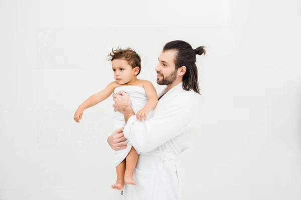 Dad looking at toddler son in towel and smiling on white — Stock Photo