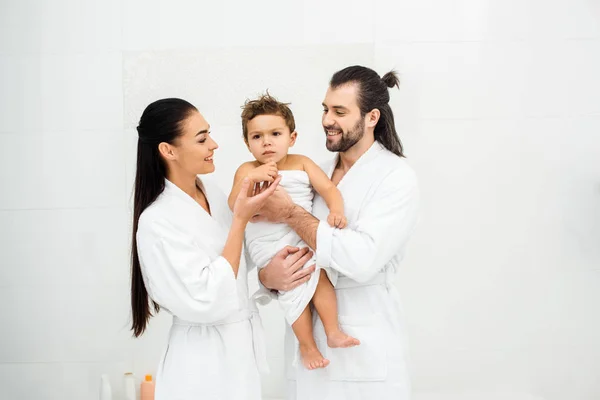 Padres mirando a su hijo en toalla blanca y sonriendo - foto de stock