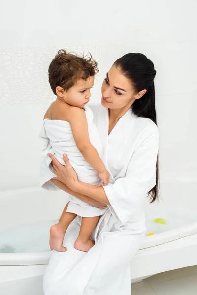 Мама дивиться на маленького сина в рушнику у ванній — стокове фото
