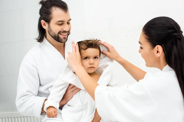 Mamá y papá mirando a su hijo en albornoz blanco y sonriendo - foto de stock