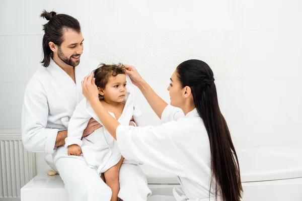 Родители сидят в ванной комнате с малышом в белом халате — стоковое фото