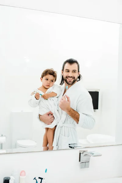 Dad and toddler son looking in mirror at home in white bathroom — Stock Photo