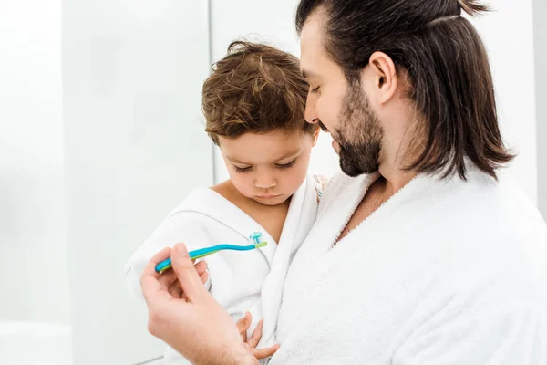 Gros plan de papa montrant brosse à dents avec dentifrice pour tout-petit fils — Photo de stock