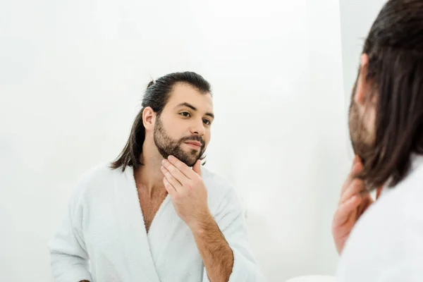 Bonito homem tocando barba e olhando no espelho — Fotografia de Stock