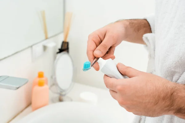 Close up of male hands holding toothpaste and toothbrush near sink — Stock Photo