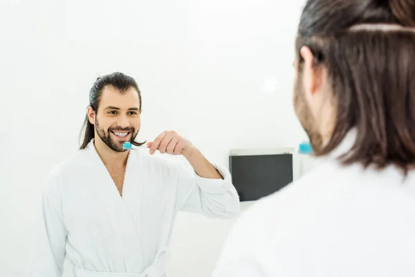 Handsome adult man in white bathrobe brushing teeth in bathroom — Stock Photo