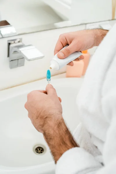 Cropped view of male hands adding toothpaste on toothbrush in bathroom — Stock Photo