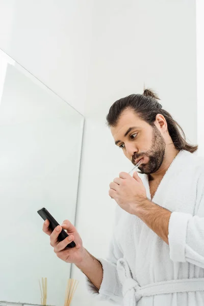 Schöner erwachsener Mann, der morgens Zähne putzt und das Smartphone benutzt — Stockfoto