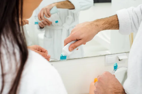 Recortado vista de hombre añadiendo pasta de dientes en mujer cepillo de dientes - foto de stock