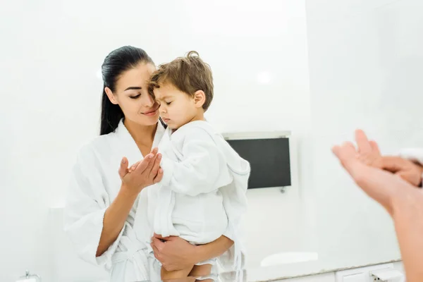 Mother in white bathrobe gently holding son hand — Stock Photo