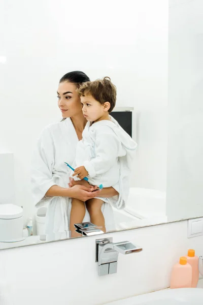 Mother and son in white bathrobes brushing teeth together — Stock Photo