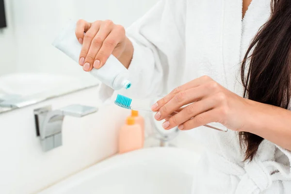 Primer plano de las manos femeninas añadiendo pasta de dientes en el cepillo de dientes - foto de stock