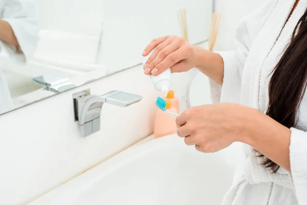 Vista cortada de mãos femininas adicionando pasta de dentes na escova de dentes no banheiro — Fotografia de Stock