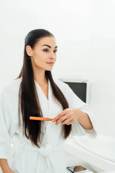 Beautiful woman combing long hair with hairbrush in bathroom — Stock Photo