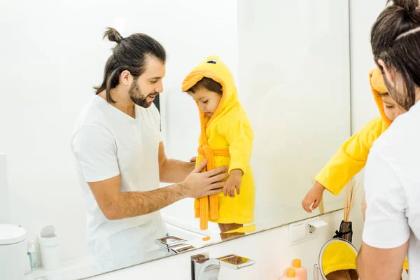Alegre papá tocando niño hijo en amarillo albornoz - foto de stock