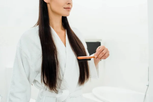 Vista recortada de la mujer peinando el pelo largo con cepillo de pelo en el baño - foto de stock