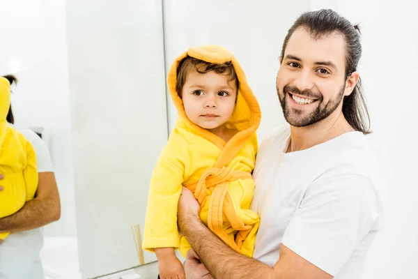 Heureux souriant père tenant fils en peignoir jaune — Photo de stock