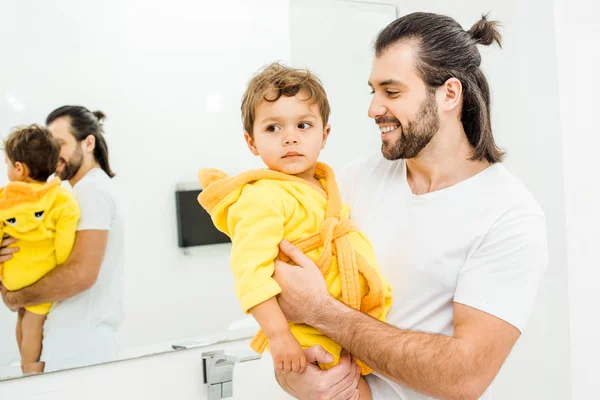 Cheerful dad holding toddler son in yellow bathrobe — Stock Photo