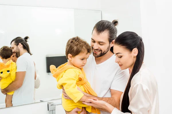 Tender young parents holding cute son in yellow bathrobe — Stock Photo