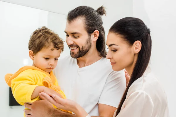 Tender young parents holding cute son in yellow bathrobe — Stock Photo